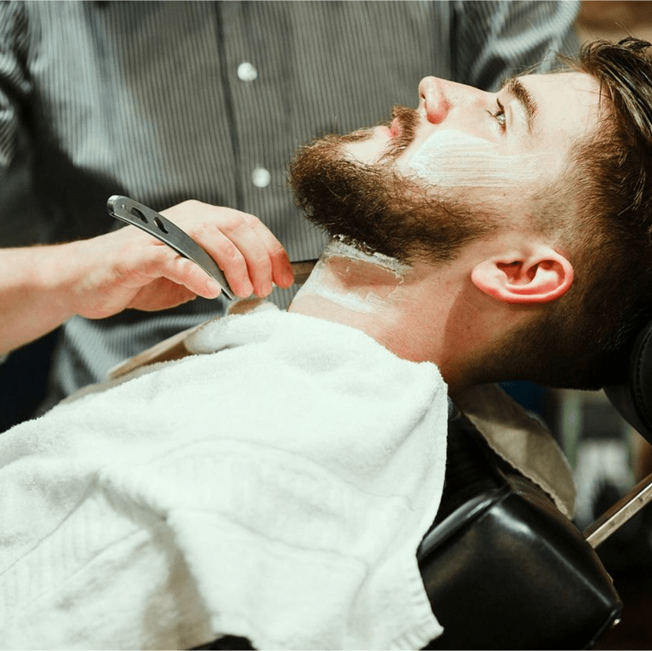 A man getting his beard shaved by another person.